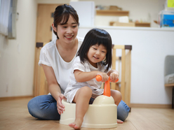 A mom sitting behind her daughter, who is sitting on a potty training toilet.