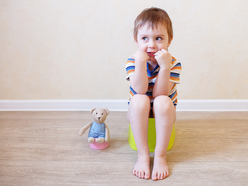 A toddler boy sitting on a potty training toilet, next to a stuffed bear on a mini toilet